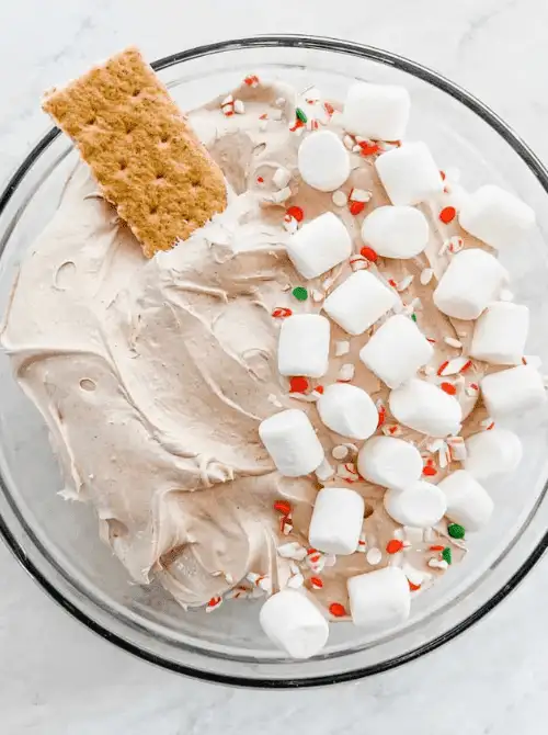 Creamy peppermint and marshmallow dessert dip served in a glass bowl with a graham cracker for dipping — a festive addition to any party dips for the holidays. This easy dessert dip is topped with crushed candy and mini marshmallows, perfect for Christmas gatherings or winter celebrations.