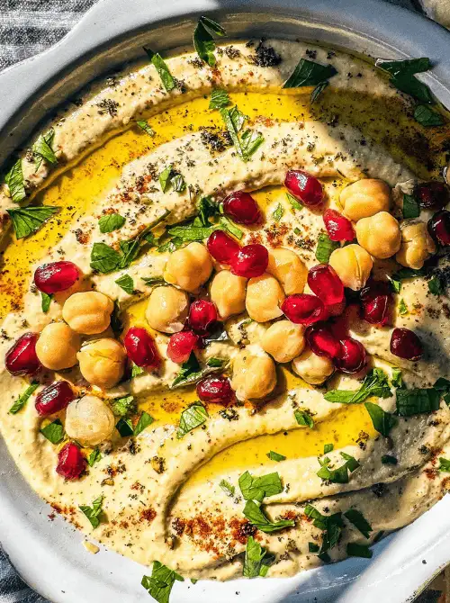 Creamy hummus topped with chickpeas, pomegranate seeds, olive oil, and herbs, a vibrant choice for Party Dips for the Holidays with Global Twists.