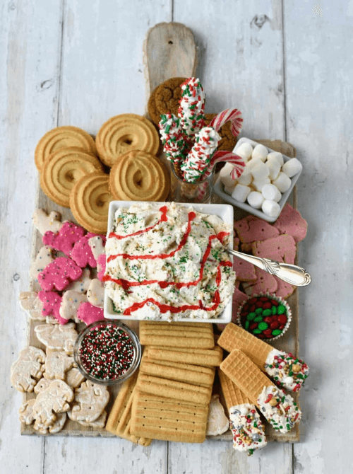 Festive dessert dip board with cookies, crackers, sprinkles, and candy canes arranged around a Christmas dip, a fun make-ahead Christmas appetizer idea and a creative option for Christmas party food ideas.