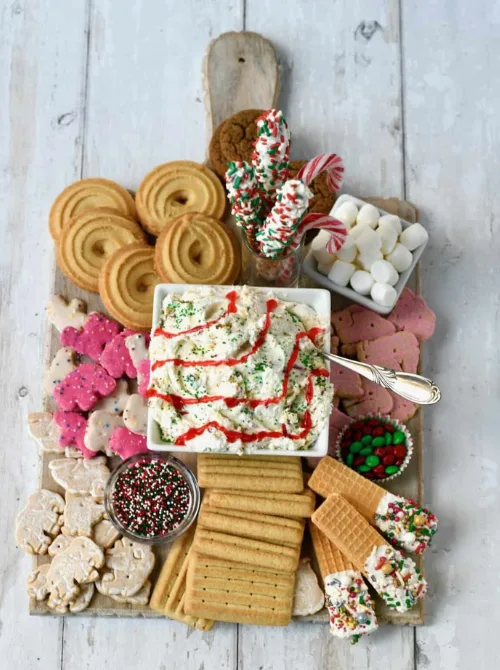 Festive dessert dip board with cookies, crackers, sprinkles, and candy canes arranged around a Christmas dip, a fun make-ahead Christmas appetizer idea and a creative option for Christmas party food ideas.
