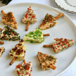 Festive tree-shaped cheese appetizer bites with pretzel sticks arranged on a white plate, topped with colorful herbs and peppers — a fun example of make-ahead Christmas appetizers and easy Christmas party food ideas.