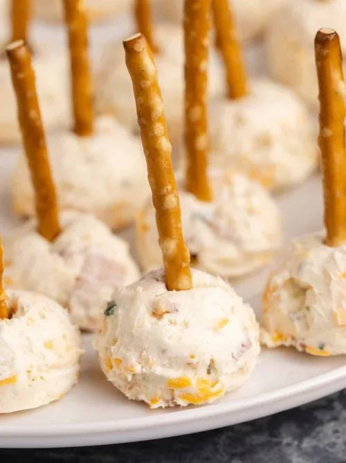 Mini cheese balls with pretzel stick handles served on a platter, a fun and affordable option for make-ahead Christmas appetizers and easy Christmas party food ideas.