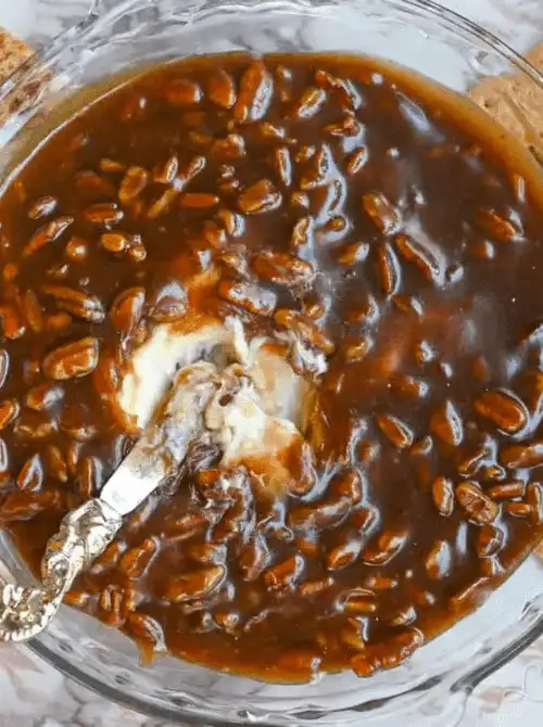 A rich and gooey easy dessert dip made with caramel and chopped pecans, served warm in a glass dish with a silver spreading knife. Perfect for party dips for the holidays, this indulgent sweet treat pairs beautifully with graham crackers or fruit for festive gatherings.