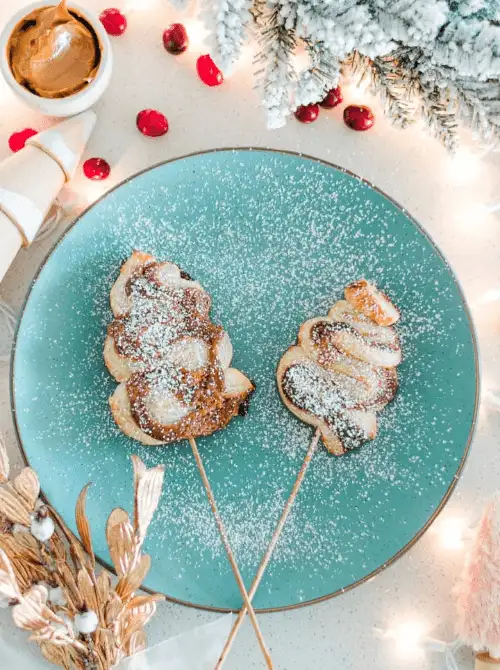 Christmas tree–shaped puff pastry sticks dusted with powdered sugar on a teal plate, a festive and fun option for make-ahead Christmas appetizers and easy Christmas party food ideas.