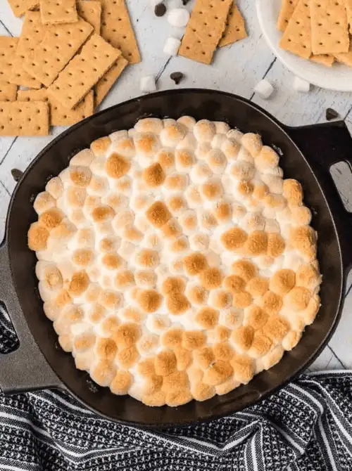 Golden, toasted marshmallow s’mores dip baked in a cast-iron skillet, surrounded by graham crackers for dipping — a cozy and crowd-pleasing idea for party dips for the holidays. This easy dessert dip adds a warm, nostalgic touch to any holiday gathering or family celebration.