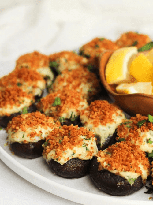 Stuffed mushrooms with golden breadcrumb topping served with lemon wedges on a white platter, a savory option for make-ahead Christmas appetizers and popular Christmas party food ideas.