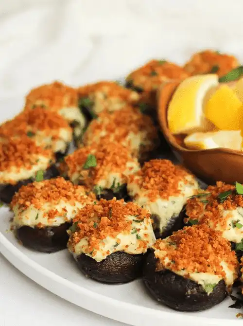 Stuffed mushrooms with golden breadcrumb topping served with lemon wedges on a white platter, a savory option for make-ahead Christmas appetizers and popular Christmas party food ideas.