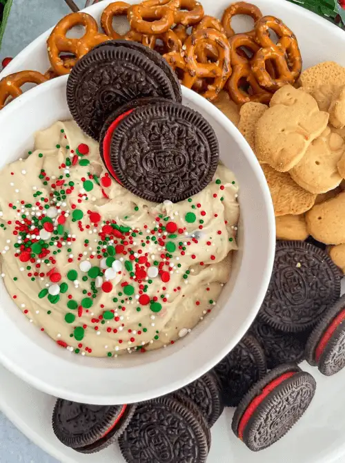 Festive Christmas cookie dip topped with red, green, and white sprinkles, served with holiday Oreos, pretzels, and cookies — a fun and colorful idea for party dips for the holidays. This easy dessert dip adds sweetness and cheer to any Christmas dessert table or holiday gathering.
