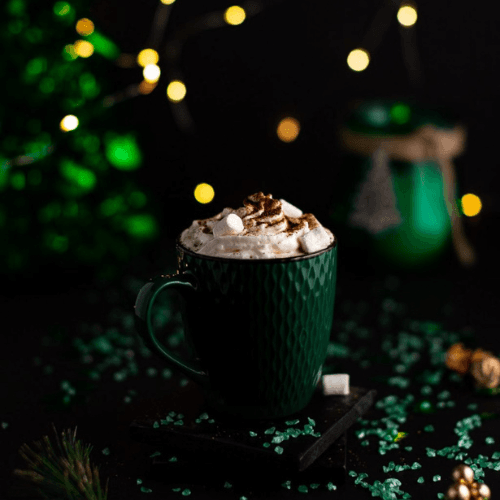 Baileys hot chocolate topped with whipped cream and cocoa in a green mug, a cozy holiday drink perfect for Christmas morning breakfast featured alongside casseroles and quiche recipes.