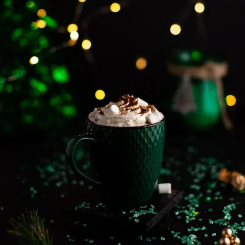 Baileys hot chocolate topped with whipped cream and cocoa in a green mug, a cozy holiday drink perfect for Christmas morning breakfast featured alongside casseroles and quiche recipes.