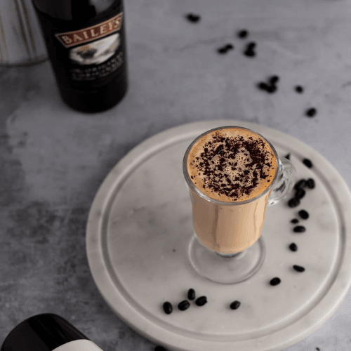 Baileys latte topped with cocoa powder and coffee beans, a festive and creamy drink to enjoy with Christmas morning breakfast featured alongside casseroles and quiche recipes.