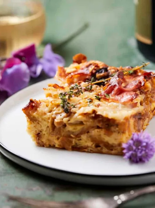 Slice of French onion croissant casserole with herbs on a white plate, an elegant and savory option for Christmas morning breakfast featured in casseroles and quiche recipes.