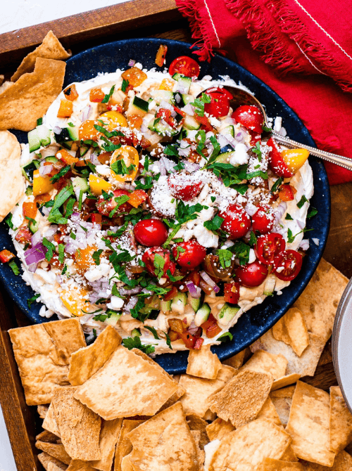 Layered Greek dip topped with chopped vegetables, feta, and fresh herbs, served with pita chips as one of the last minute dips for dips for your Super Bowl party