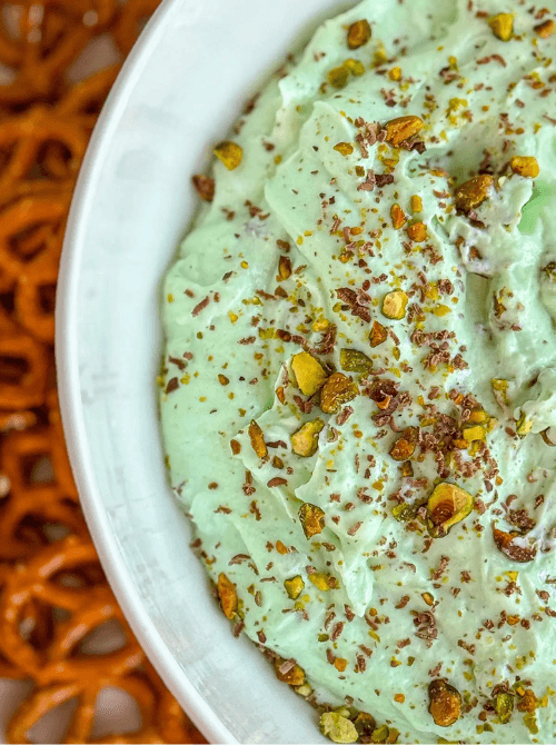 Creamy pistachio yogurt dip topped with chopped pistachios, shown in a white bowl with pretzels nearby as one of the last minute dips for dips for your Super Bowl party