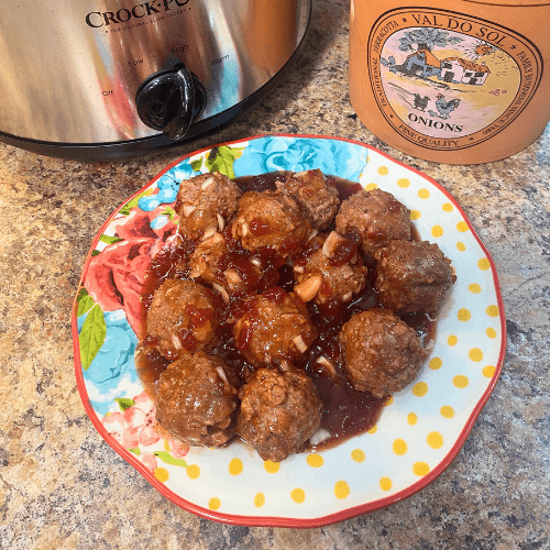 Sweet chili cranberry crockpot meatballs served on a floral plate, coated in a glossy cranberry and sweet chili sauce, shown beside a slow cooker as an easy holiday appetizer for a crowd.