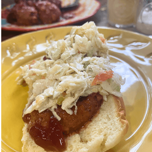 Meatball sandwich topped with sweet chili cranberry sauce and creamy coleslaw on a yellow plate