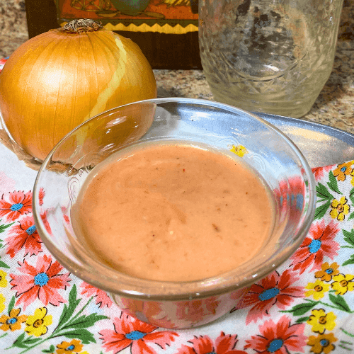 Homemade sweet chili cranberry mayo sauce in a glass bowl with fresh onion and rustic kitchen background.