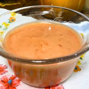 Homemade sweet chili cranberry mayo in a clear glass bowl on a floral kitchen towel.