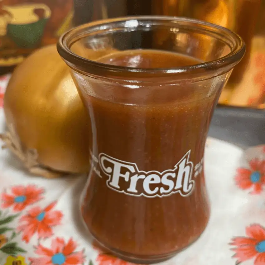 Close-up of homemade sweet chili cranberry salad dressing made with cranberry sauce and onion in a glass jar.