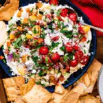 Layered Greek dip topped with chopped vegetables, feta, and fresh herbs, served with pita chips as one of the last minute dips for dips for your Super Bowl party