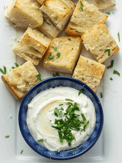 Whipped ricotta dip drizzled with olive oil and topped with fresh herbs, served with toasted garlic bread cubes as one of the last minute dips for dips for your Super Bowl party