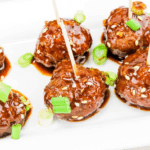 Sticky Asian-style meatballs garnished with green onions and sesame seeds, a tasty pick from easy crock pot recipes for a last minute Super Bowl party.