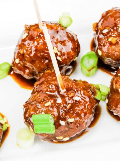 Sticky Asian-style meatballs garnished with green onions and sesame seeds, a tasty pick from easy crock pot recipes for a last minute Super Bowl party.