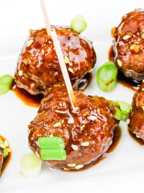 Sticky Asian-style meatballs garnished with green onions and sesame seeds, a tasty pick from easy crock pot recipes for a last minute Super Bowl party.