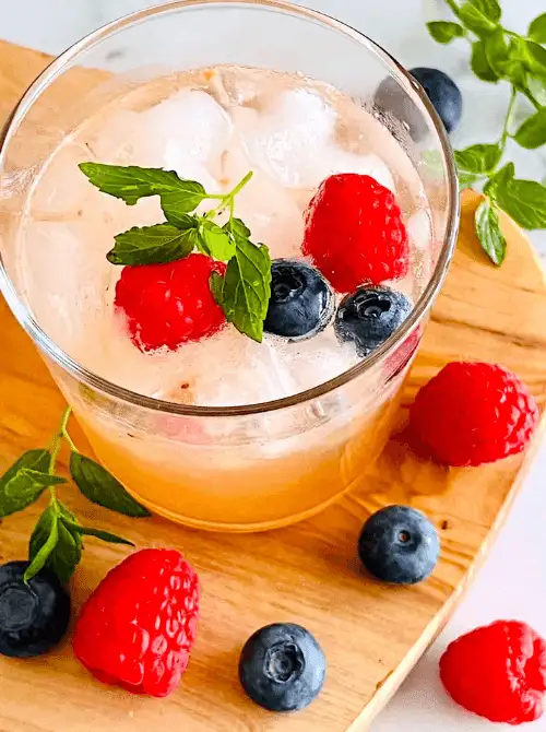 Close-up of a berry ginger mocktail served for a Galantine's Day Party, showcasing easy mocktail ideas with raspberries, blueberries, and mint over ice.