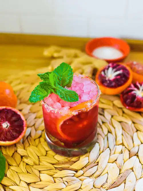Close-up of a blood orange mocktail served for a Galantine's Day Party, showcasing easy mocktail ideas with mint garnish and citrus slices on a woven placemat.