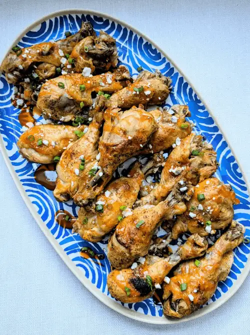 Buffalo chicken drumsticks glazed in sauce and sprinkled with green onions on a platter, part of easy crock pot recipes for a last minute Super Bowl party.