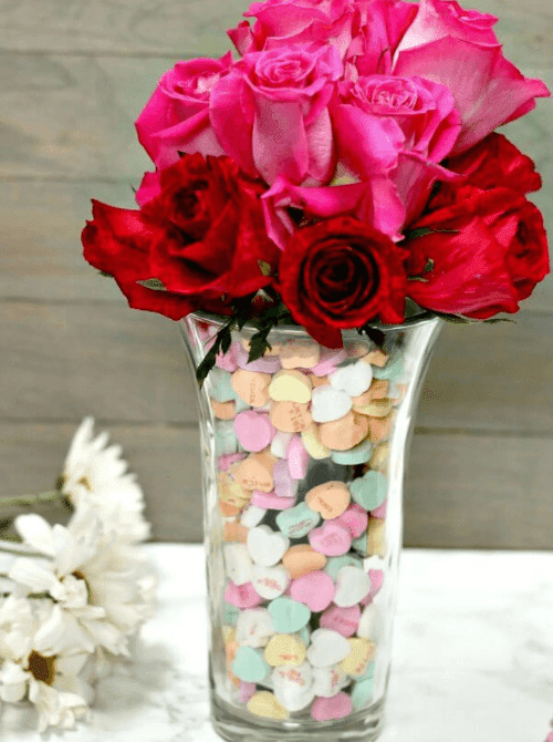 Glass vase filled with conversation hearts and pink roses, easy Valentine’s DIY craft using Dollar Tree supplies.