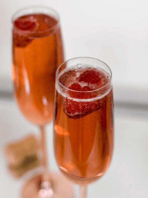 Pink Cocktail Ideas for a Galentine’s Day Party featuring raspberry mimosas in champagne flutes with fresh raspberries
