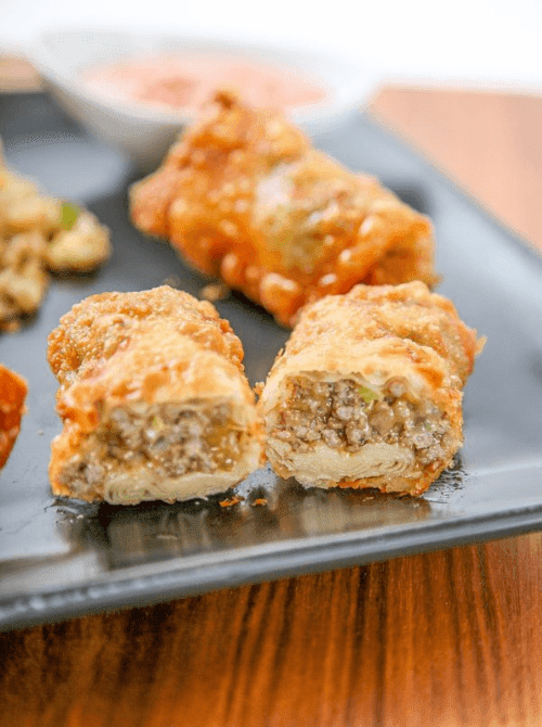 Crispy cheeseburger egg rolls with a beef filling, served as an easy cheap tailgate food and simple Super Bowl appetizer.