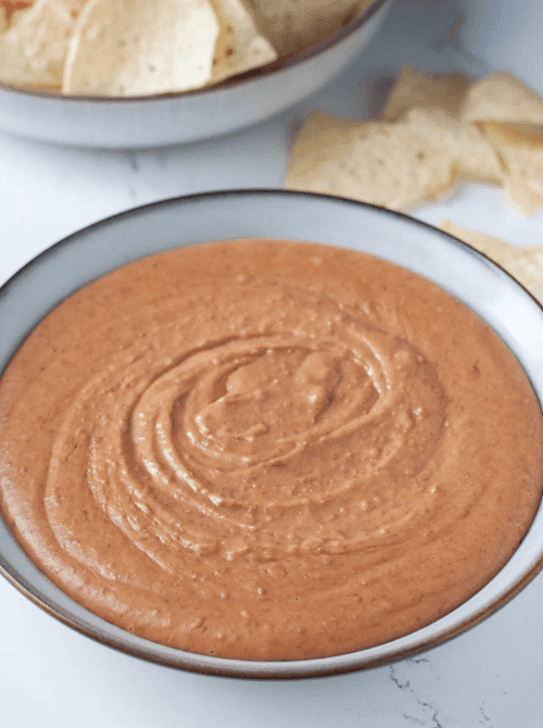 Homemade refried bean dip ready for dipping, a crowd-friendly cheap tailgate food and simple Super Bowl appetizer.