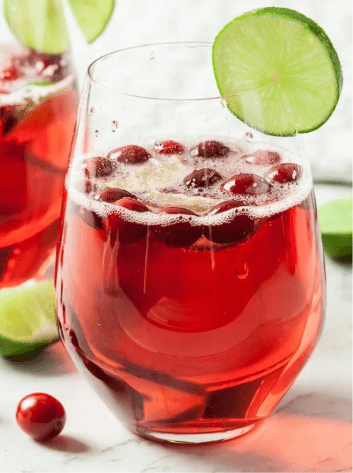 Pink Cocktail Ideas for a Galentine’s Day Party featuring a cranberry cocktail with fresh cranberries and lime garnish in a stemless glass