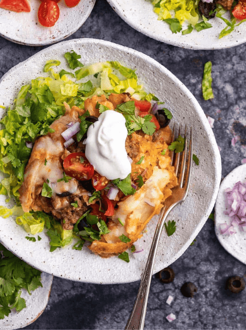 Crock pot taco casserole bowl topped with sour cream, lettuce, tomatoes, and olives, part of easy crock pot recipes for a last minute Super Bowl party.