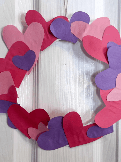 Heart wreath made with cardstock cutouts in red, pink, and purple, easy Valentine’s DIY craft using Dollar Tree supplies.