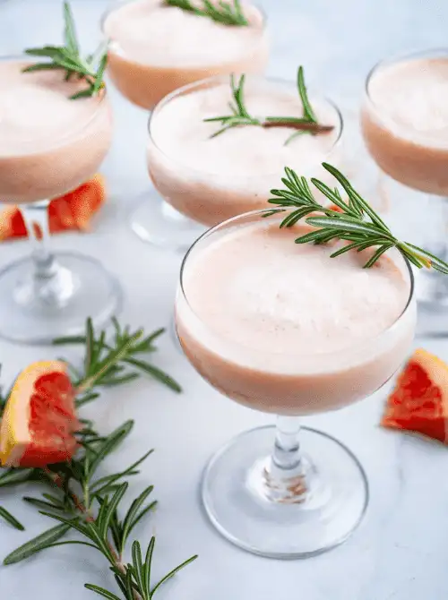 Close-up of grapefruit mocktails served for a Galantine's Day Party, showcasing easy mocktail ideas with rosemary sprigs in coupe glasses and citrus slices nearby.
