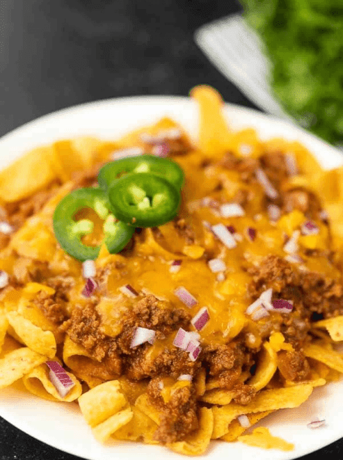 Crock pot Frito pie topped with jalapeños, shredded cheese, and red onion, a fun choice from easy crock pot recipes for a last minute Super Bowl party.