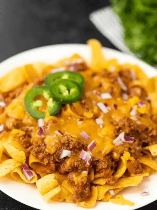Crock pot Frito pie topped with jalapeños, shredded cheese, and red onion, a fun choice from easy crock pot recipes for a last minute Super Bowl party.