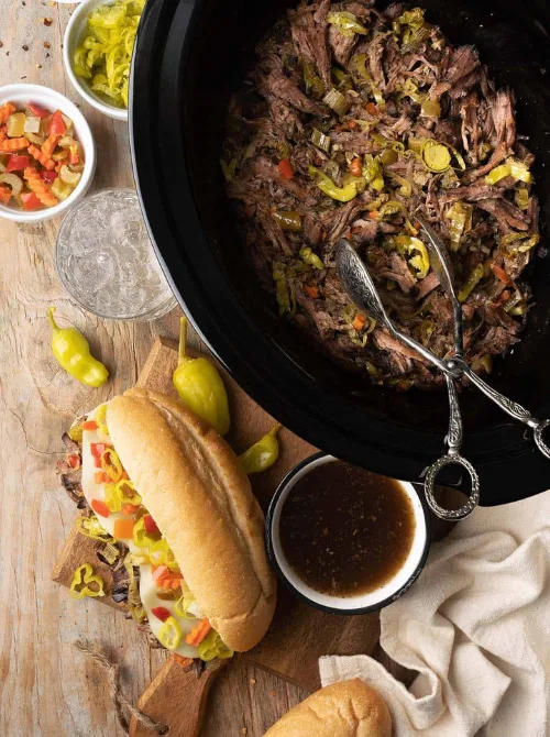 Slow cooker Italian beef with peppers and sliced rolls ready for sandwiches, featured in easy crock pot recipes for a last minute Super Bowl party.