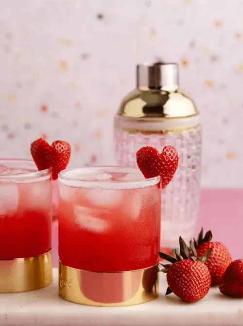 Pink Cocktail Ideas for a Galentine’s Day Party featuring strawberry cocktails served over ice with heart-shaped strawberry garnish and gold-rimmed glasses