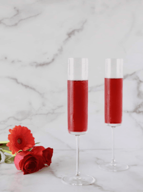 Pink Cocktail Ideas for a Galentine’s Day Party featuring cranberry prosecco cocktails served in champagne flutes with fresh red florals