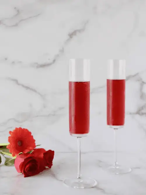 Pink Cocktail Ideas for a Galentine’s Day Party featuring cranberry prosecco cocktails served in champagne flutes with fresh red florals