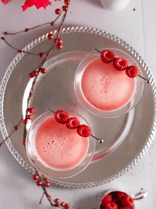 Pink Cocktail Ideas for a Galentine’s Day Party featuring two raspberry martinis in coupe glasses with fresh raspberry garnish on a silver tray