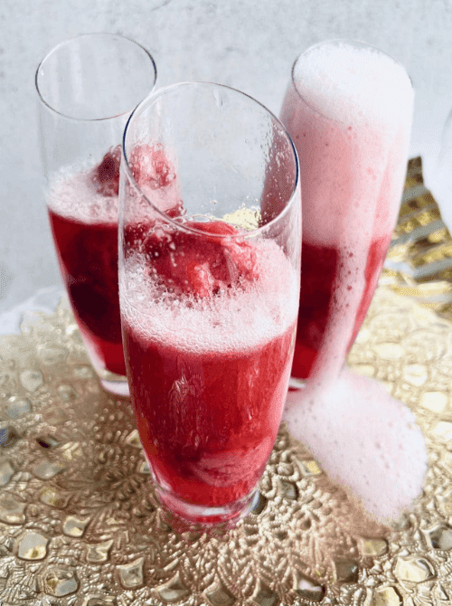 Pink Cocktail Ideas for a Galentine’s Day Party featuring sparkling strawberry cocktails bubbling over in tall champagne flutes