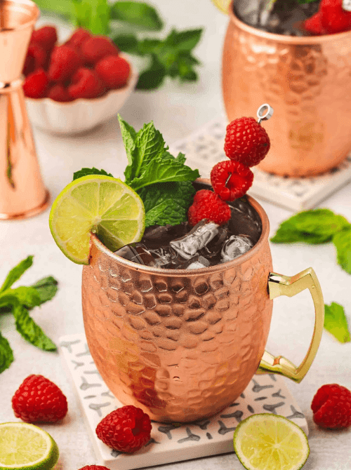Pink Cocktail Ideas for a Galentine’s Day Party featuring a raspberry Moscow mule in a copper mug with fresh mint, lime, and raspberry garnish