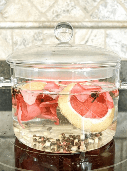 Glass pot filled with grapefruit slices, rose petals, and spices simmering on the stove, a cozy Valentine’s DIY craft made on a Dollar Tree budget.