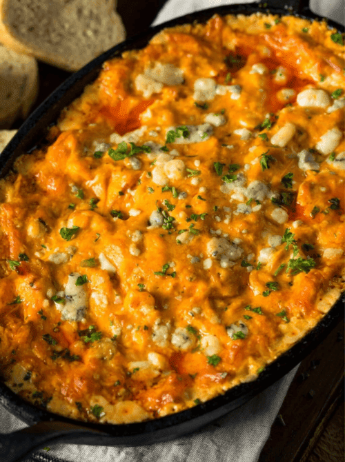 Skillet of creamy buffalo chicken dip topped with blue cheese crumbles and herbs, a great example of easy crock pot recipes for a last minute Super Bowl party.